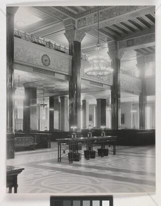 A black-and-white photograph of the interior of an ornate office lobby with inlaid floors, columns, and chandeliers.