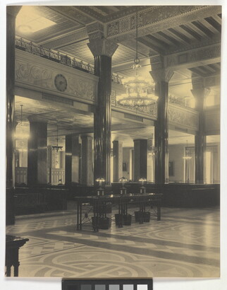 A black-and-white photograph of the interior of an ornate office lobby with inlaid floors, columns, and chandeliers.