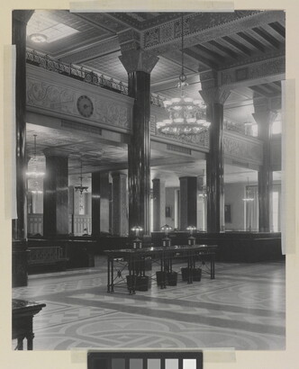 A black-and-white photograph of the interior of an ornate office lobby with inlaid floors, columns, and chandeliers.