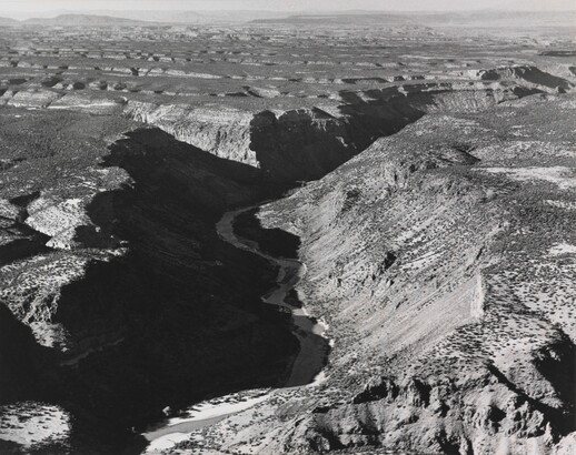 A black-and-white photograph of an aerial view of a river winding through a steep canyon.