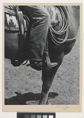 A black-and-white photograph of a person&#039;s leg in a cowboy boot, including spurs, sitting astride a horse, viewing only the horse&#039;s front quarter.