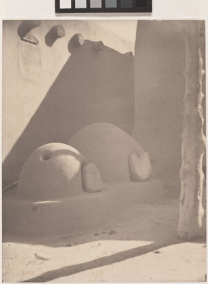 A black-and-white photograph of two beehive ovens attached to an adobe structure.