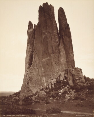 A sepia-toned photograph of a large vertical rock formation against a clear sky.