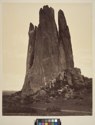 A sepia-toned photograph of a large vertical rock formation against a clear sky.