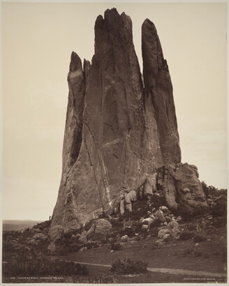 A sepia-toned photograph of a large vertical rock formation against a clear sky.