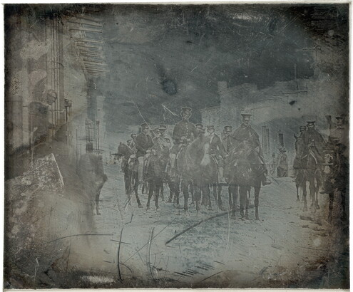 A dark, black-and-white photograph of a group of figures in military uniform on horseback on a street.