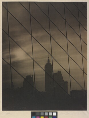 A sepia-toned photograph of a patterned grid of cables in front of a dark city skyline.