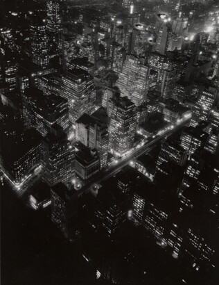 A black-and-white photograph of a bird&#039;s eye view of city lights at night.