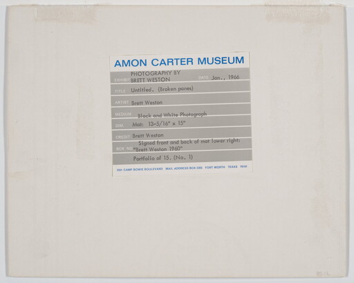 A black-and-white photograph of broken window panes in what looks like a factory building.