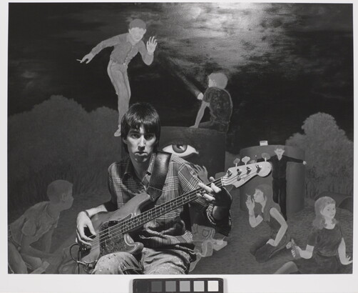 A black-and-white photograph of a young White man playing an electric guitar in front of a mural of people smoking and drinking.