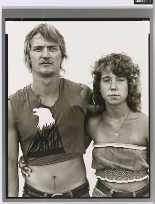A black-and-white portrait photograph of a young White man and woman, arms around each other, both wearing crop-top shirts.