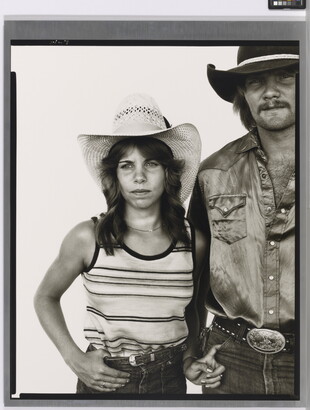 A black-and-white portrait photograph of a young White woman in a cowboy hat and striped tank top with one hand hooked into her jeans and the other hooked into the pocket of a White man in a cowboy hat and satin button-up shirt.