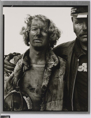 A black-and-white portrait photograph of two men, one with his arm around the other, both covered in coal dust and wearing dirty clothes.