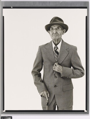 A black-and-white portrait photograph of an elderly White man in a hat, suit, tie, and one hand holding a cane.