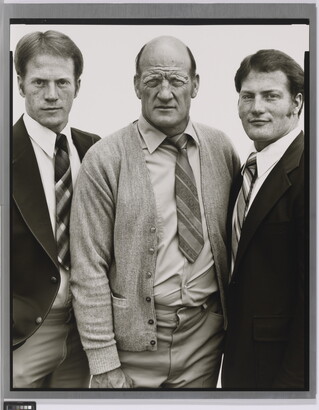 A black-and-white portrait photograph of three White men, two younger on the left and right and the one in the center middle-aged and bald, all wearing suits and ties.