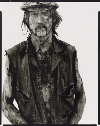 A black-and-white portrait photograph of a White man covered in dirt and oil wearing a vest and hard hat.