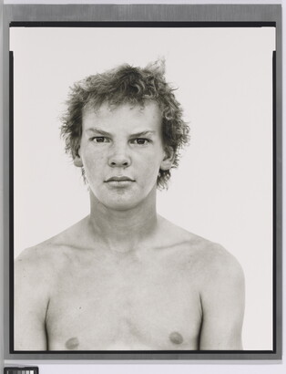 A black-and-white portrait photograph of a shirtless White teenage boy with messy hair.