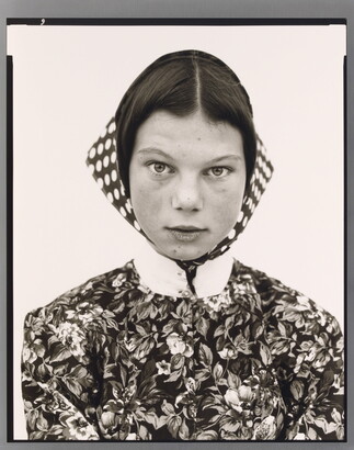 A black-and-white portrait photograph of a teenage White girl wearing a high-collared, floral print blouse and a polka-dotted head scarf.