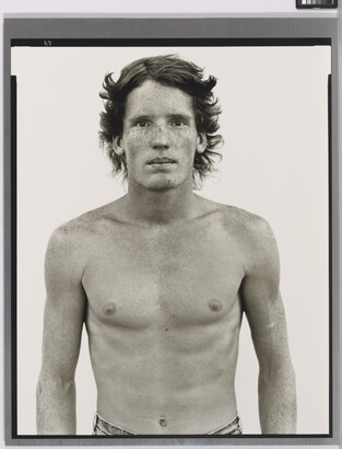A black-and-white portrait photograph of a shirtless young White man with freckles across his face and shoulders.