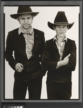 A black-and-white portrait photograph of a young White man and boy, both wearing cowboy hats, dark jackets, and plaid shirts.