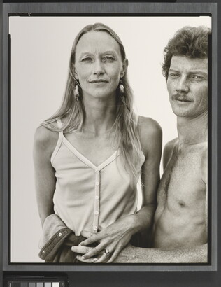 A black-and-white portrait photograph of a thin White woman with long hair wearing camisole as a shirtless White man with curly hair and a moustache holds her waist.