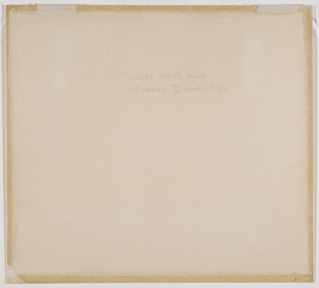 A black-and-white photograph of a nude, fair-skinned woman lying facedown in the sand with her head resting on her crossed arms.