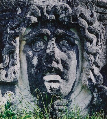 A color photograph of an ancient stone carving of a woman's face with snakes for hair.