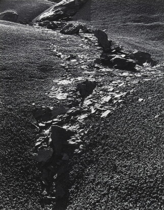 A black-and-white photograph of rocks and rock flakes bisecting a gravelly slope.