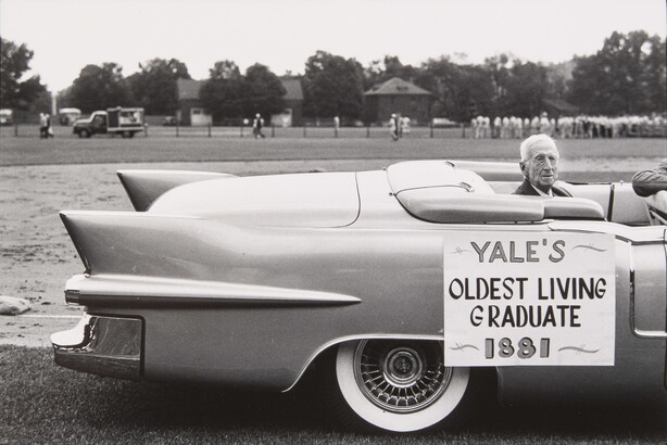 A black-and-white photograph of an elderly White man seated in the back of a convertible; a sign on the car reads, &quot;Yale&#039;s oldest living graduate, 1881.&quot;