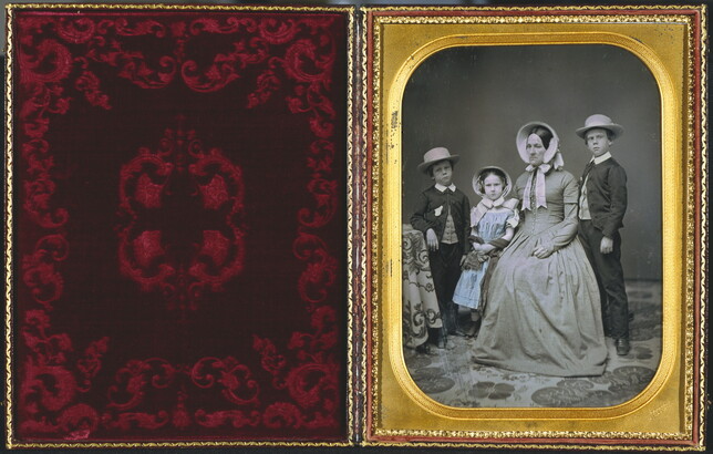 A hand-painted black-and-white formal portrait photograph in a gold frame of a White woman sitting with two boys and a girl standing around her.