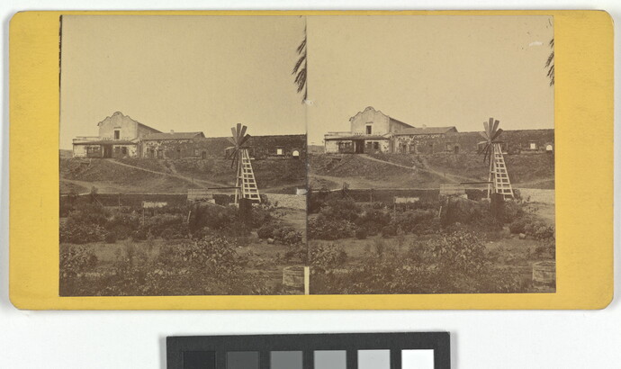 Two almost identical sepia-toned photographs side by side an adobe building on a hill with a windmill in the foreground.