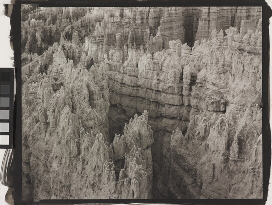 A black-and-white landscape photograph of a view of banded rock formations in a canyon.
