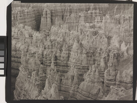 A black-and-white landscape photograph of a view of banded rock formations in a canyon.