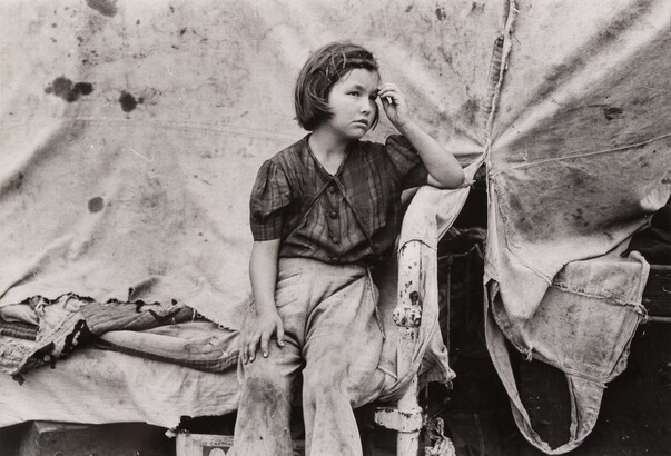 A black-and-white photograph of a young White girl wearing dirty clothes, one hand held up to her forehead, sitting in front of a canvas tent.
