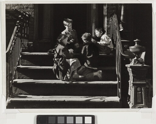A black-and-white photograph of four children playing together on concrete steps with iron railings that cast striped shadows across them.