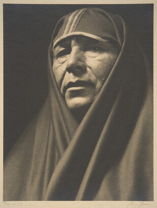 A sepia-toned portrait photograph of an adult Indigenous person with a shawl covering their head and shoulders.