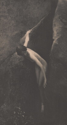 A sepia-toned photograph of a nude White woman emerging from between two large boulders.