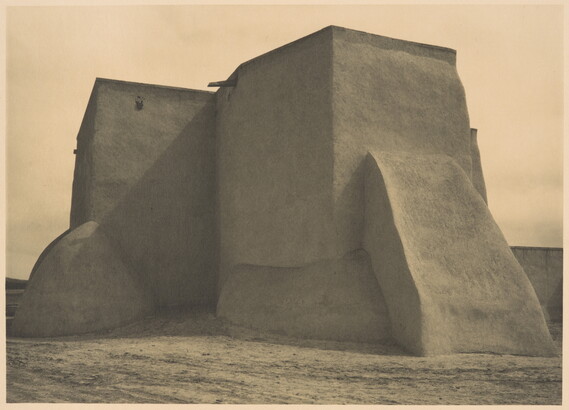 A black-and-white photograph of an adobe church from the back.