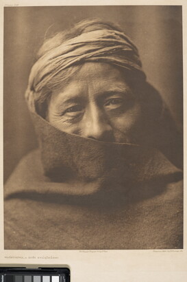 A sepia-toned portrait photograph of an older Indigenous person wearing headband with their face partially covered by what looks like a blanket.