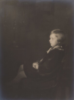 A black-and-white, soft-focus photograph of a young White girl with bobbed hair, sitting in profile.