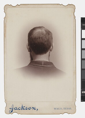A black-and-white studio portrait photograph of the back of the head, from the neck up, of a man with short hair.