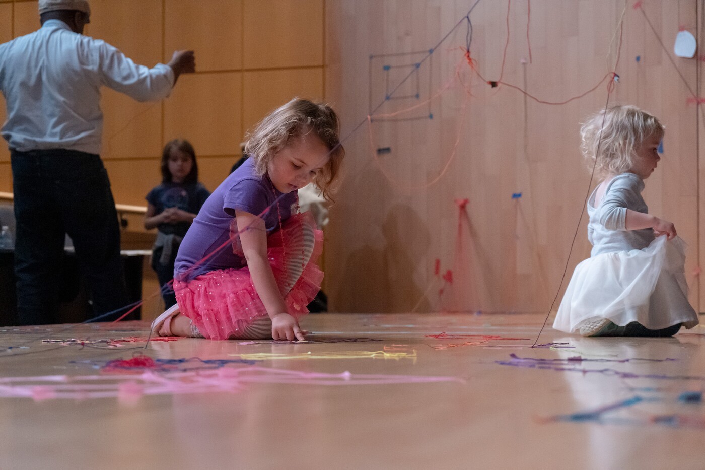 Two toddlers play with colored string on the floor of a gallery.