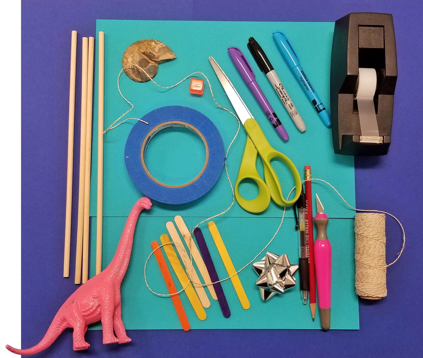 Art supplies and a pink brontosaurus laid out on a table.