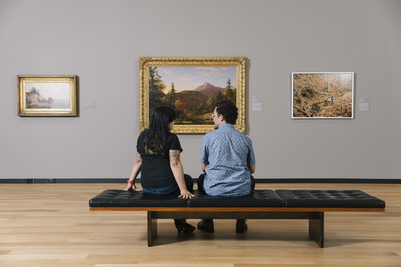 Two adults sit next to each other on a bench in a Carter gallery looking at art.
