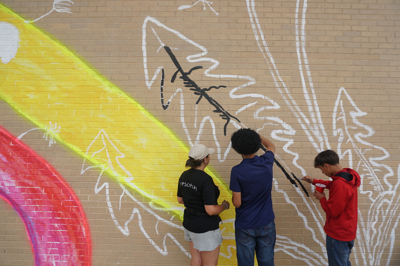 Middle school students paint a mural on to a brick wall.