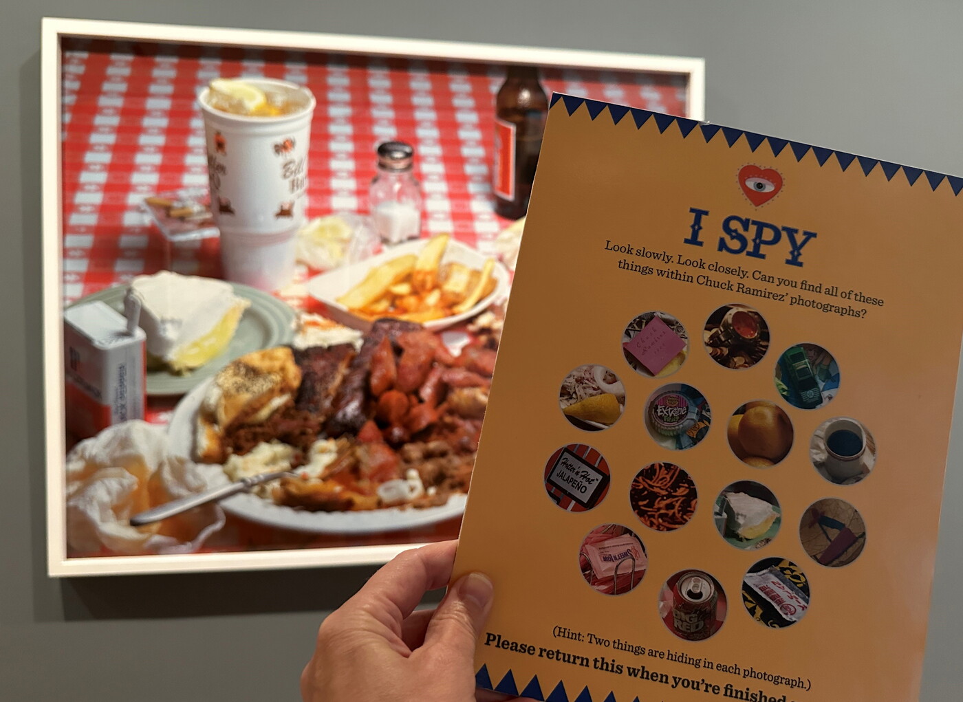 A person holds up an "I Spy" activity card in front of a photograph in a Carter gallery.