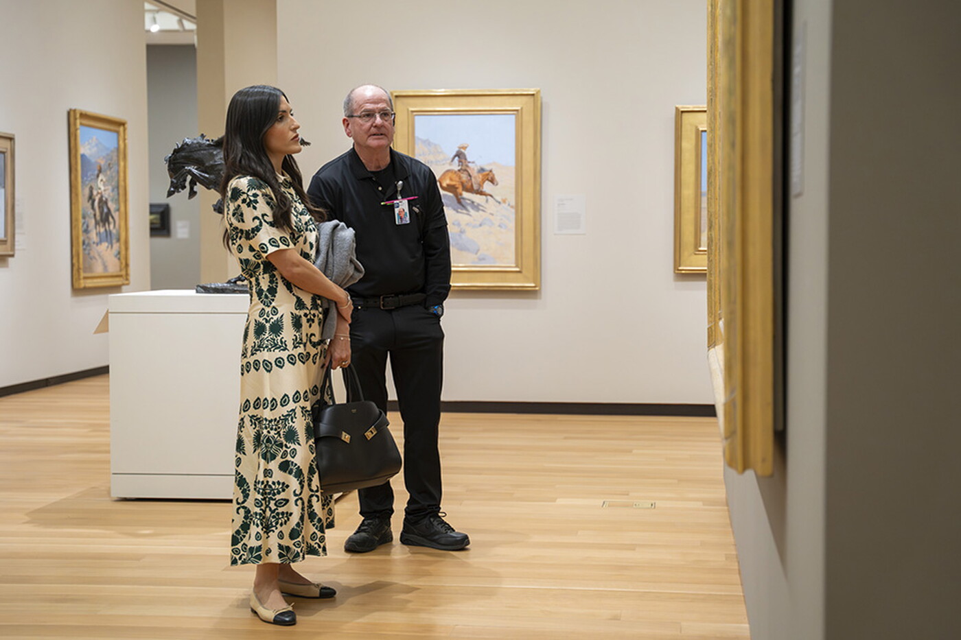 A White woman looks at artwork in a Carter gallery as an older White man wearing black stands nearby.