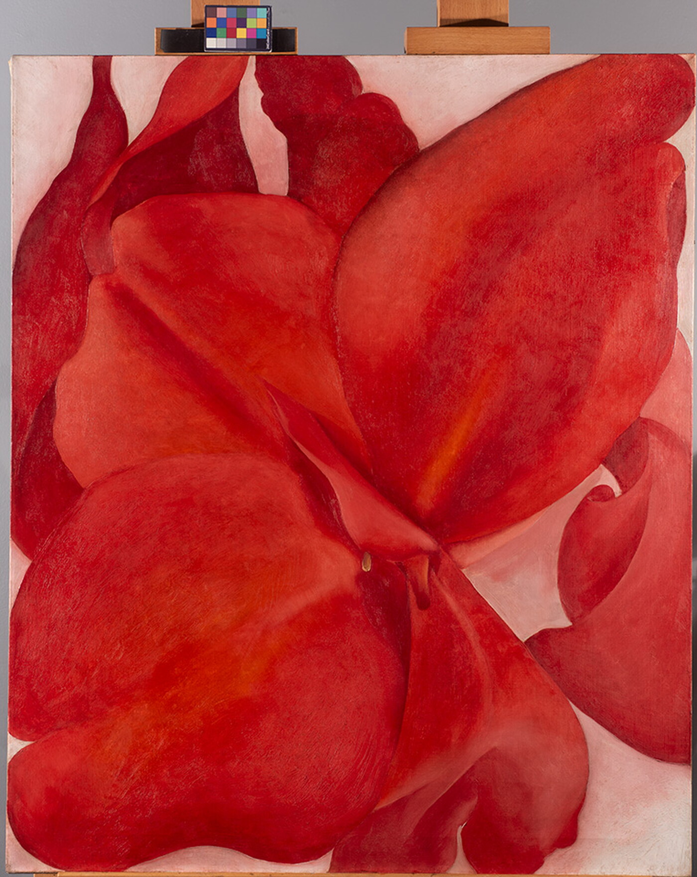 An oil painting on an easel of an extreme close-up, abstracted view of a red flower.