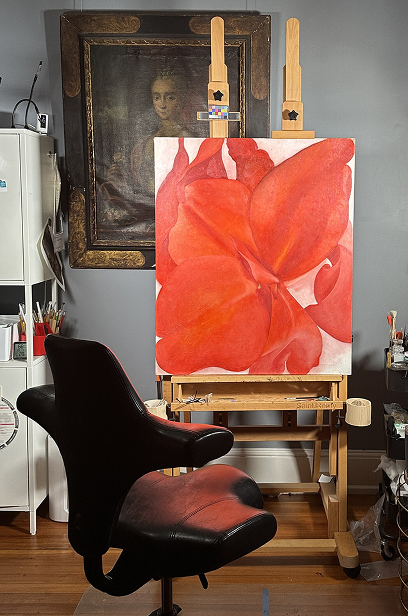 A painting of a red flower sits on an easel in a studio.
