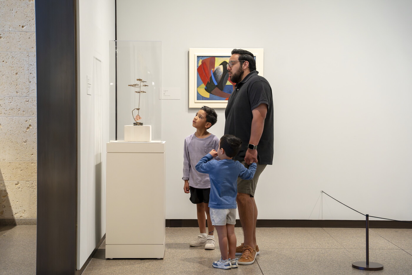 A White man holds the hands of two children as they look at art in a Carter gallery.